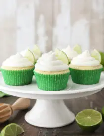 Key Lime Cupcakes sitting on a cake stand with lime wedges in frosting.