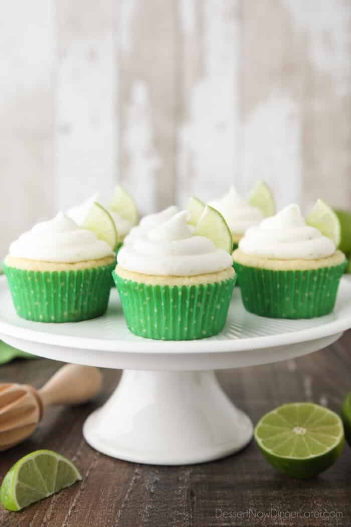 Key Lime Cupcakes sitting on a cake stand with lime wedges in frosting.