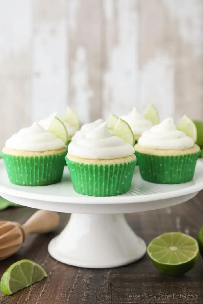 Key Lime Cupcakes sitting on a cake stand with lime wedges in frosting.