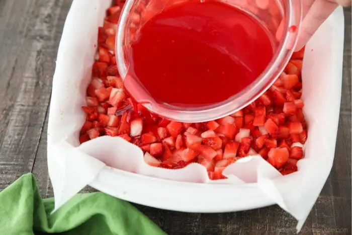 Pouring strawberry jello mixture over fresh strawberries.