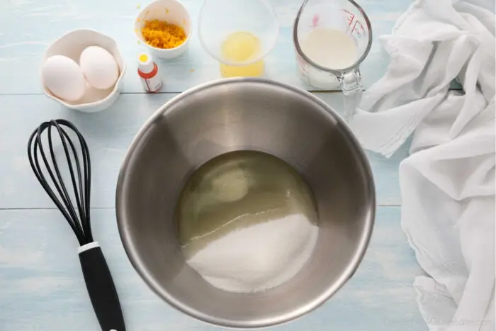 Sugar and oil in a bowl, with eggs, yellow gel food coloring, lemon zest, lemon juice, and buttermilk on the side.