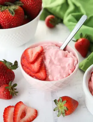 Strawberry Fluff Jello Salad in a bowl with sliced strawberries on top and a spoon inserted into the dessert.