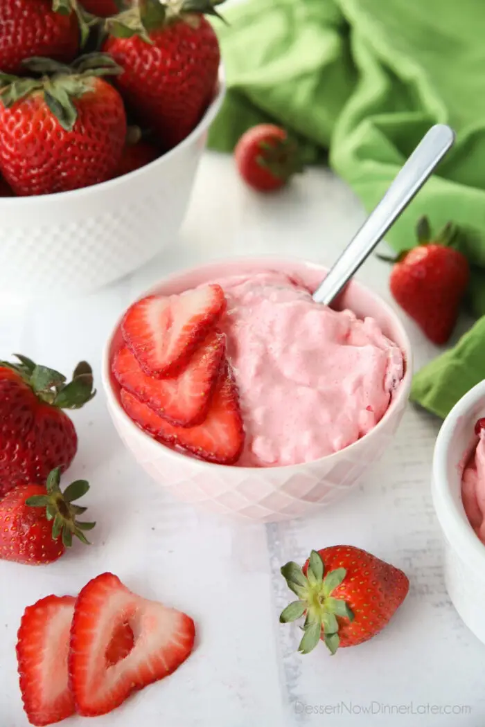 Strawberry Fluff Jello Salad in a bowl with sliced strawberries on top and a spoon inserted into the dessert.