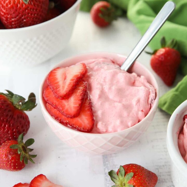 Strawberry Fluff Jello Salad in a bowl with sliced strawberries on top and a spoon inserted into the dessert.