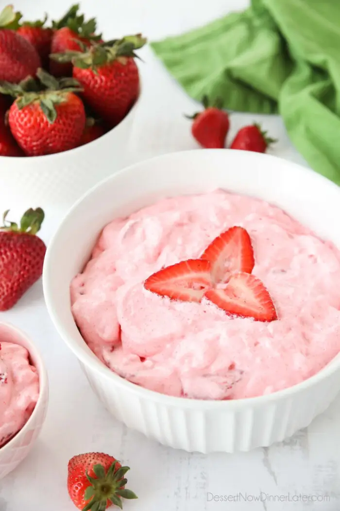 Bowl full of strawberry jello salad with sliced strawberries on top and extra strawberries on the side.