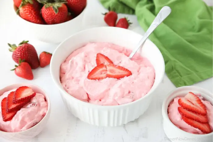 Angled view of three bowls of strawberry fluff jello salad topped with sliced strawberries.