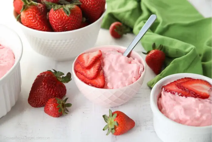 Strawberry Fluff Jello Salad in a bowl with sliced strawberries on top and a spoon inserted into the dessert.