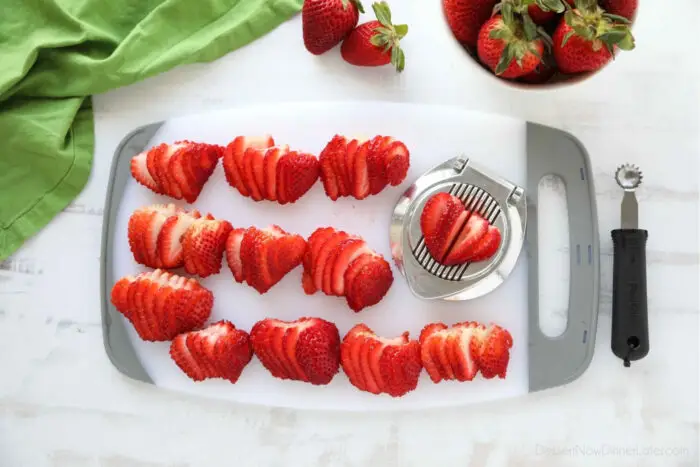 Cutting board full of strawberries that have been sliced with an egg slicer.