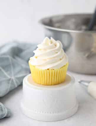 Focus is on a cupcake piled high with whipped cream cheese frosting.
