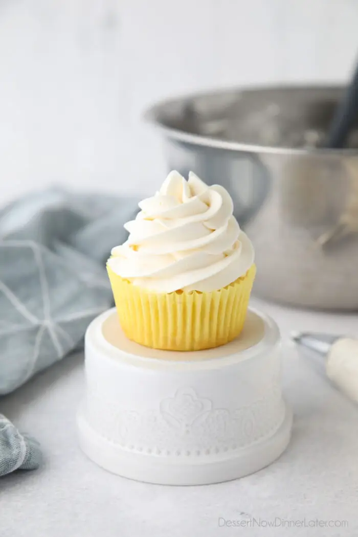 Focus is on a cupcake piled high with whipped cream cheese frosting.