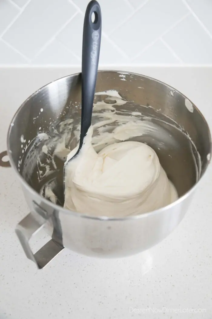 Whipped cream cheese frosting in mixing bowl with spatula.