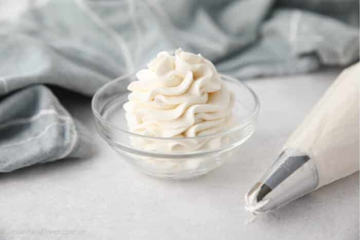 Whipped Cream Cheese Frosting piped high into a clear glass bowl.