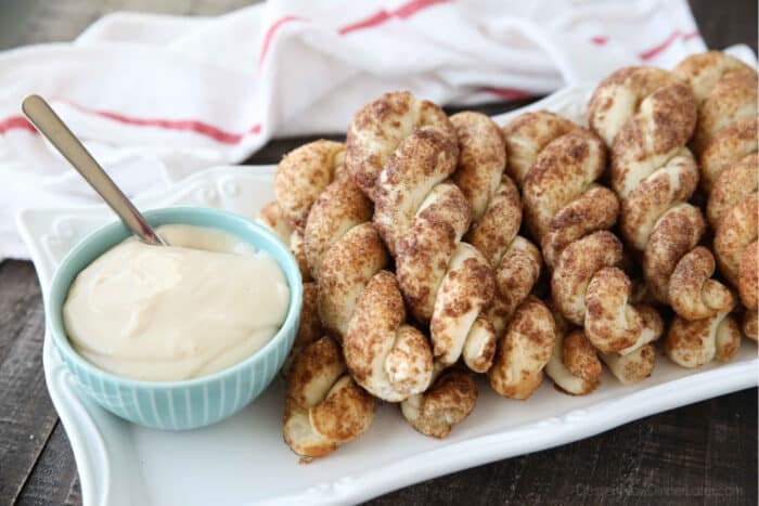 Plate full of cinnamon twists with a bowl of cream cheese dip.
