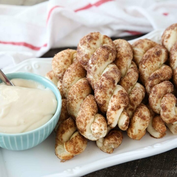 Plate full of cinnamon twists with a bowl of cream cheese dip.