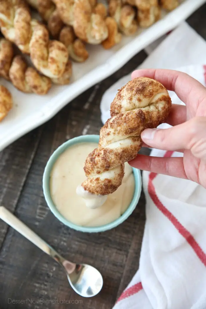 Top view of a cinnamon twist being dipped into cream cheese glaze.