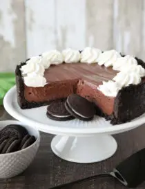 No-bake chocolate cheesecake and Oreos on a cake plate with whipped cream piped on top.