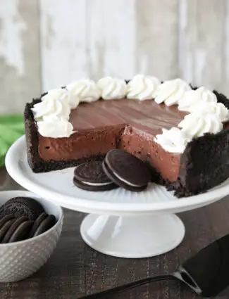 No-bake chocolate cheesecake and Oreos on a cake plate with whipped cream piped on top.