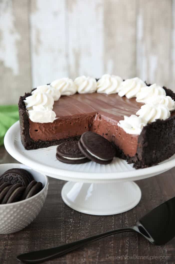 No-bake chocolate cheesecake and Oreos on a cake plate with whipped cream piped on top.