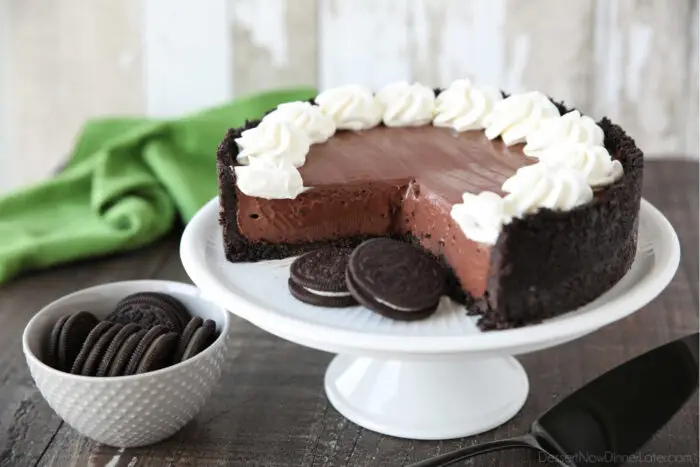 No bake chocolate cheesecake and Oreos on a cake plate with whipped cream piped on top.