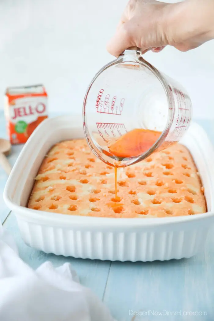 Pouring orange jello into holes of white cake.
