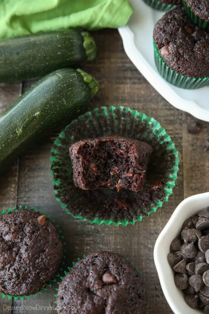 A chocolate zucchini muffin with a bite taken out showing melted chocolate chips on the inside and a moist crumb.