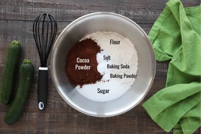 Bowl of labeled ingredients for chocolate zucchini muffins: Flour, Sugar, Cocoa Powder, Salt, Baking Soda, and Baking Powder.