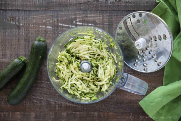 Food processor with shredding attachment taken off and shredded zucchini inside.