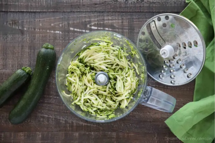 Food processor with shredding attachment taken off and shredded zucchini inside.