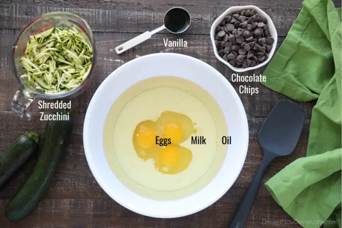 Labeled ingredients for chocolate zucchini muffins: Eggs, milk, oil, vanilla, shredded zucchini, and chocolate chips.