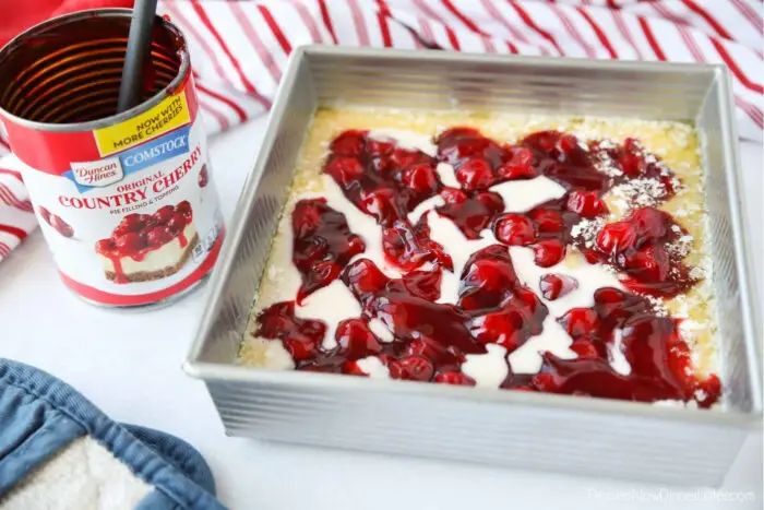 Cake batter and cherry pie filling on top of melted butter before baking.