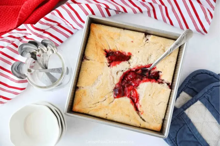 Top view of cherry cobbler in a square baking dish with a serving spoon.
