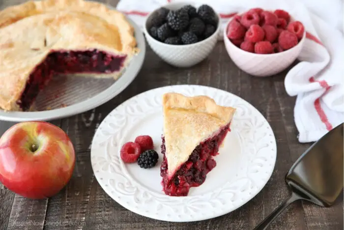 Slice of razzleberry pie on plate with raspberries and blackberries.