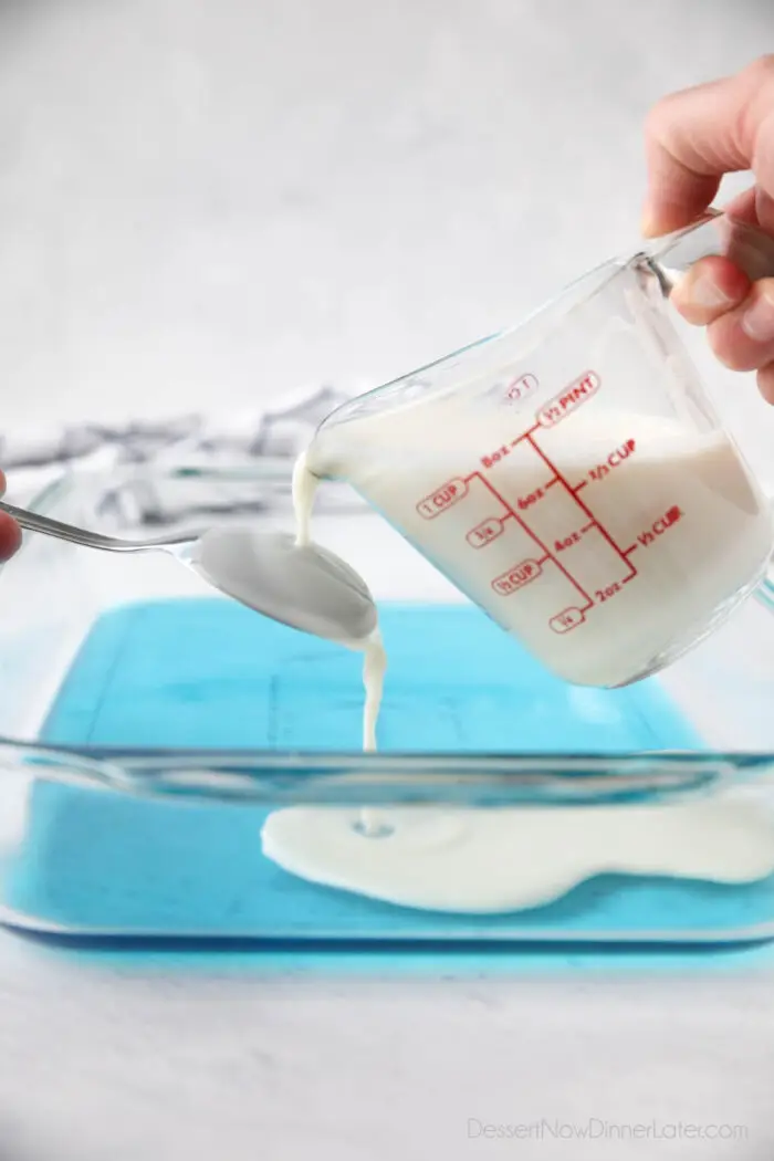 Layering the jello. Pouring white gelatin over the back of a spoon onto the blue jello.