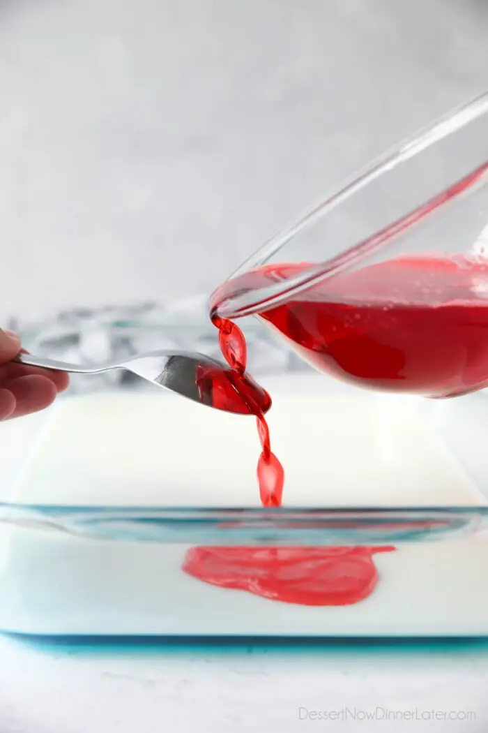 Layering the jello. Pouring red jello over the back of a spoon onto the white gelatin.