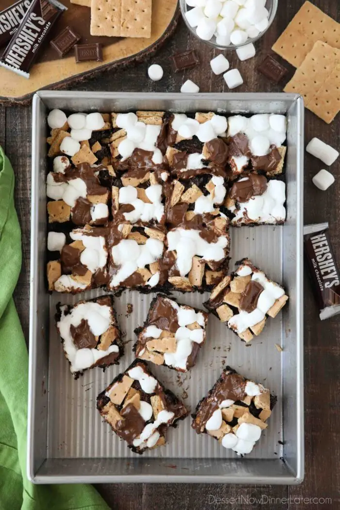 S'mores Brownies with graham crackers, mini marshmallows, and Hershey's chocolate bars in a pan, cut into squares with a few missing, and other brownies separated from the rest.