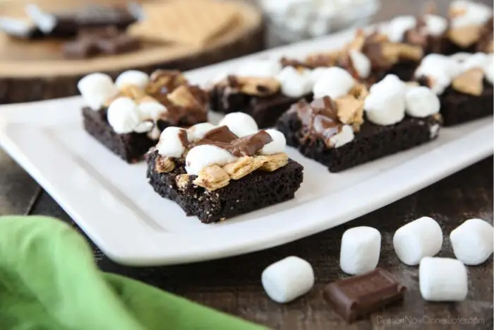 Close up side view of dark chocolate brownies topped with smores ingredients: graham crackers, marshmallows, and chocolate.