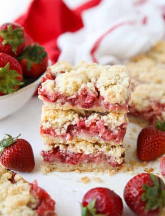 Three strawberry crumb bars stacked on top of each other surrounded by fresh whole strawberries.