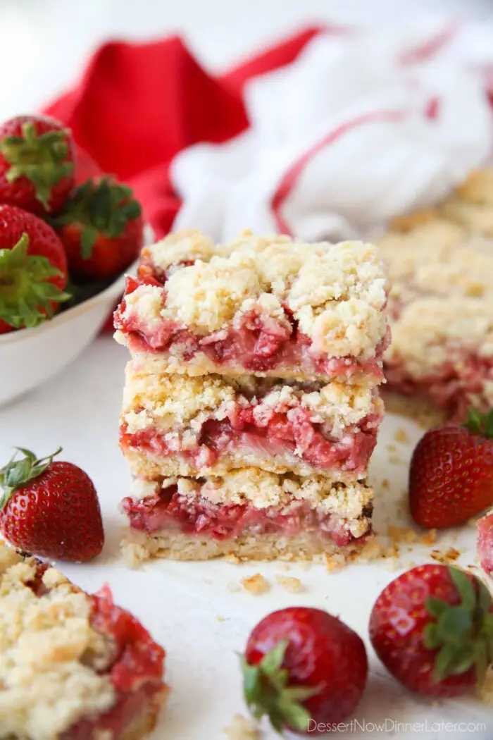 Three strawberry crumb bars stacked on top of each other surrounded by fresh whole strawberries.