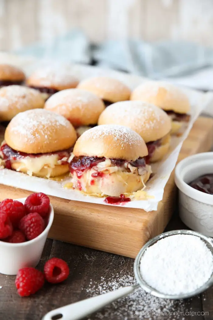 Monte Cristo Sliders on parchment paper with ham, turkey, Swiss cheese, and raspberry preserves inside of dinner rolls with powdered sugar on top.