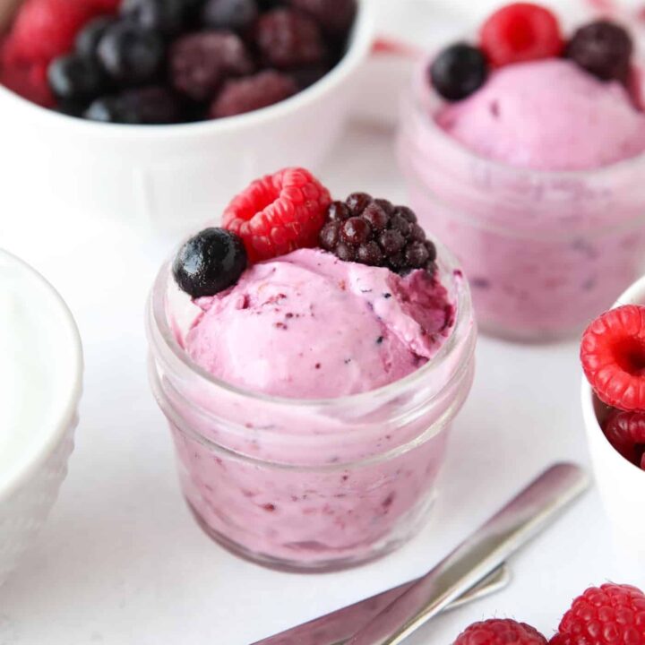 Scoop of berry frozen yogurt in a small glass mason jar with fresh berries on top.