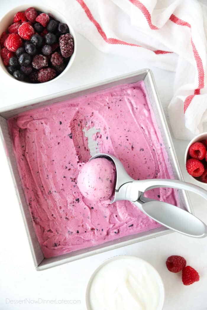 Homemade berry frozen yogurt in a shallow square dish being scooped with an ice cream scoop.