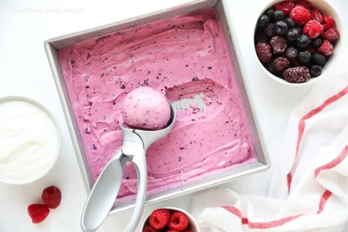 Homemade berry frozen yogurt in a shallow square dish being scooped with an ice cream scoop.