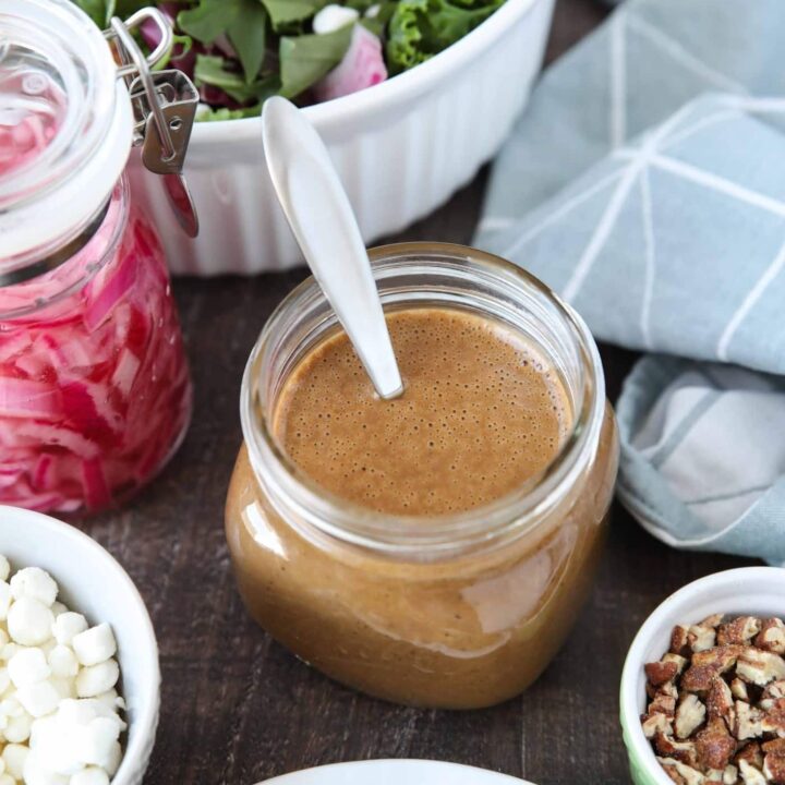 Focus on a glass mason jar of thick and creamy balsamic dressing with a spoon inside.