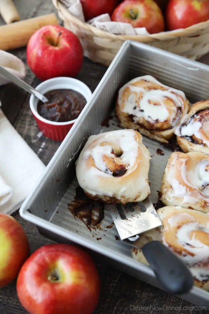 Scooping an apple butter cinnamon roll out of the pan with a spatula.