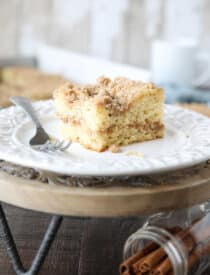 Close up of a slice of sour cream coffee cake on a plate with a line of cinnamon streusel in the center of the cake and more streusel on top.