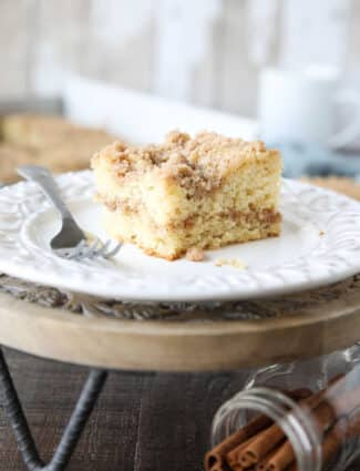 Close up of a slice of sour cream coffee cake on a plate with a line of cinnamon streusel in the center of the cake and more streusel on top.