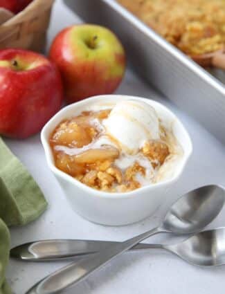 Close up of a bowl full of caramel apple dump cake and vanilla ice cream on top.