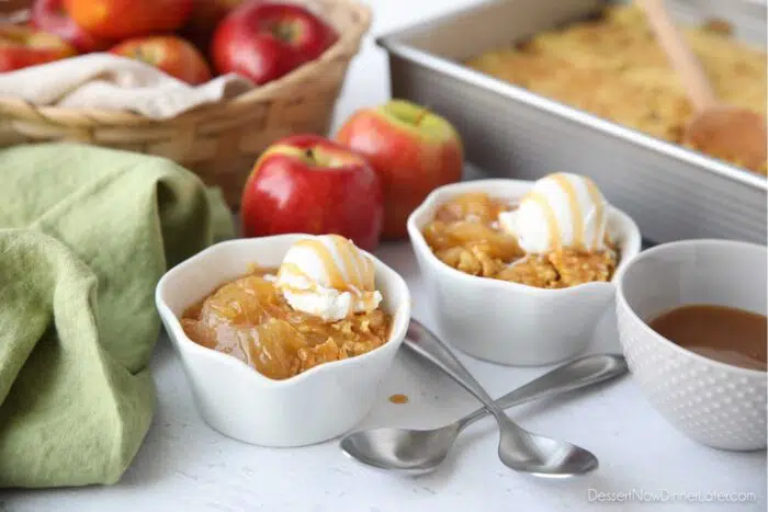 Caramel apple dump cake served up in small bowls with vanilla ice cream and caramel on top.
