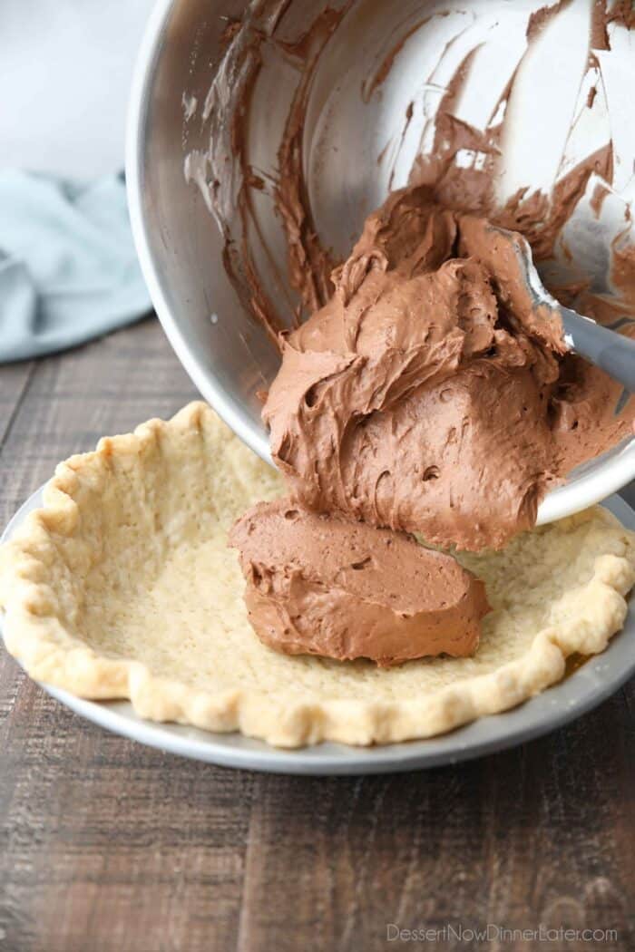 Whipped cream mixed with chocolate pudding being emptied into a baked pie crust.