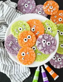 Bright colored Halloween cookies on a plate with powdered sugar cracks and candy eyeballs.